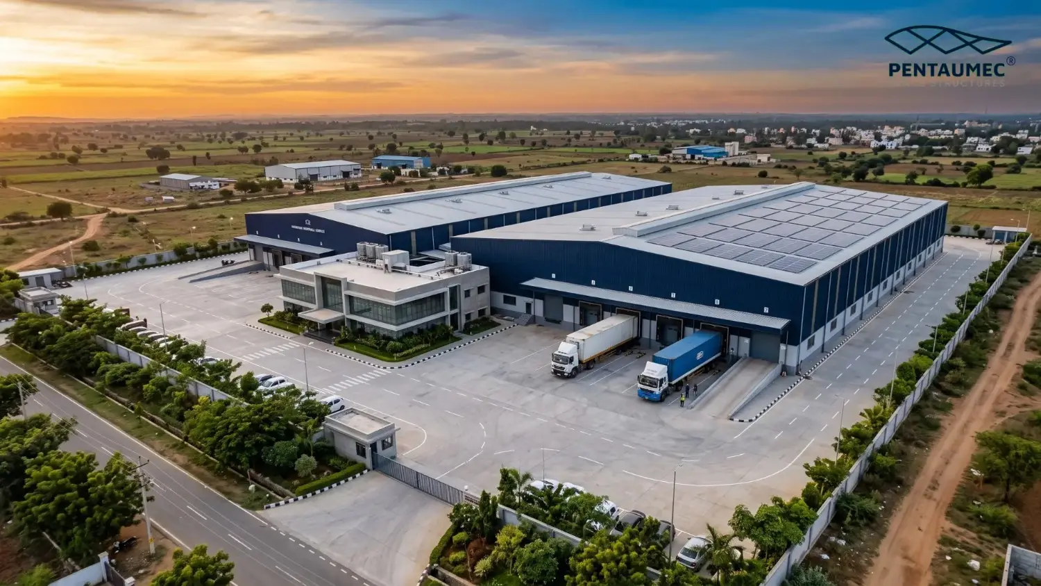 Aerial view of a Karnataka industrial zone along a national highway showing multiple PEB steel factory buildings with loading docks trucks and organised internal road network